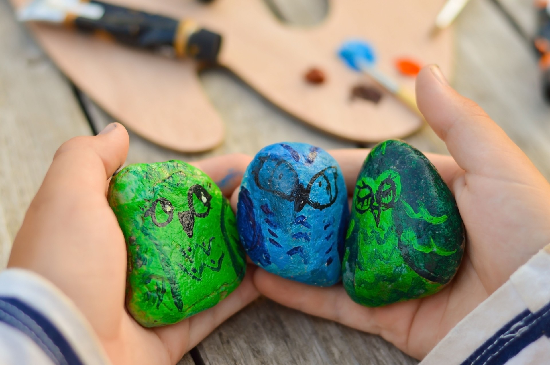 Outdoor workshop in summer. A selective focus of a schoolboy boy holding a painted flat stone in his hands. Do it yourself.